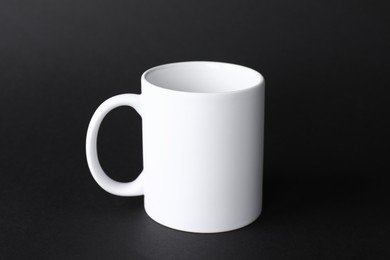 Photo of One blank white mug on black background. Mockup for design