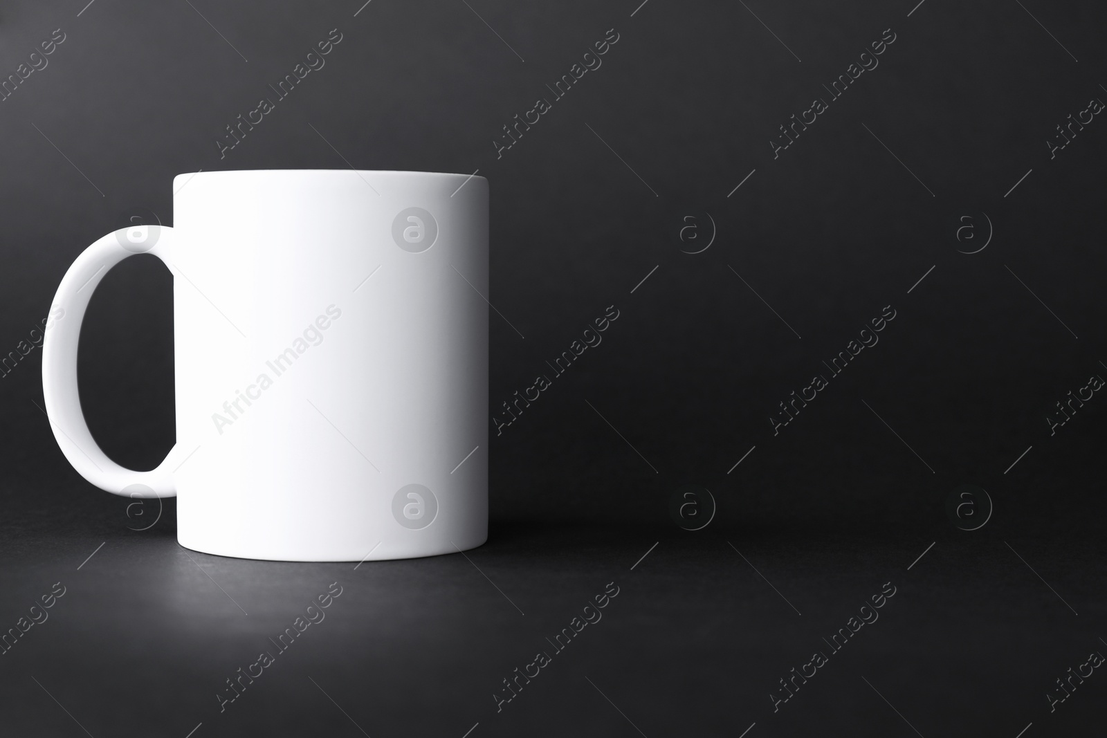 Photo of One blank white mug on black background. Mockup for design