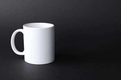 Photo of One blank white mug on black background. Mockup for design