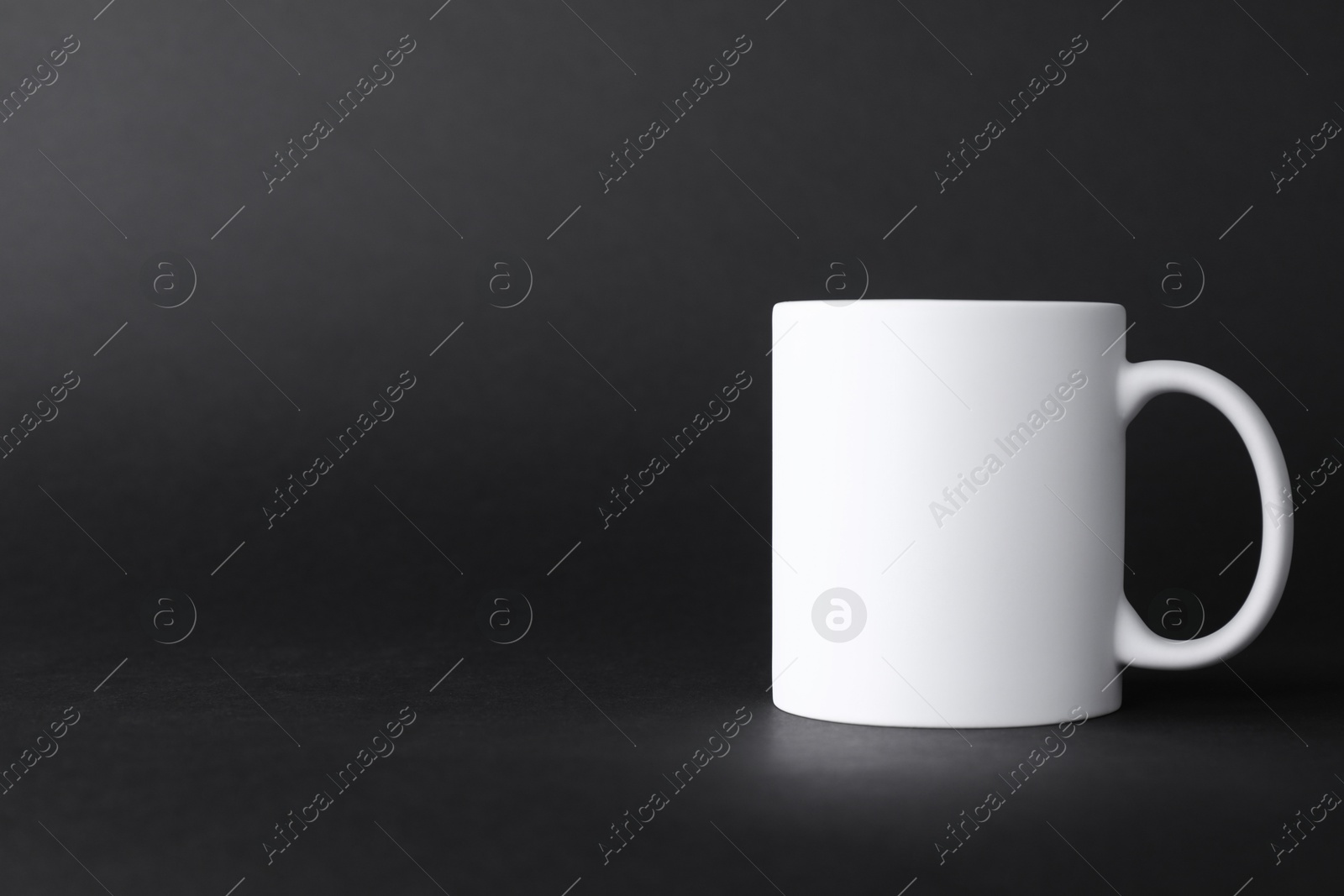 Photo of One blank white mug on black background. Mockup for design