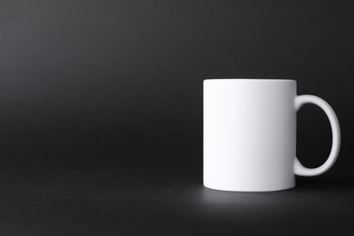 Photo of One blank white mug on black background. Mockup for design