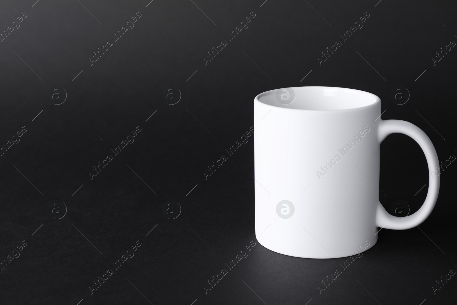 Photo of One blank white mug on black background. Mockup for design