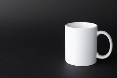 Photo of One blank white mug on black background. Mockup for design