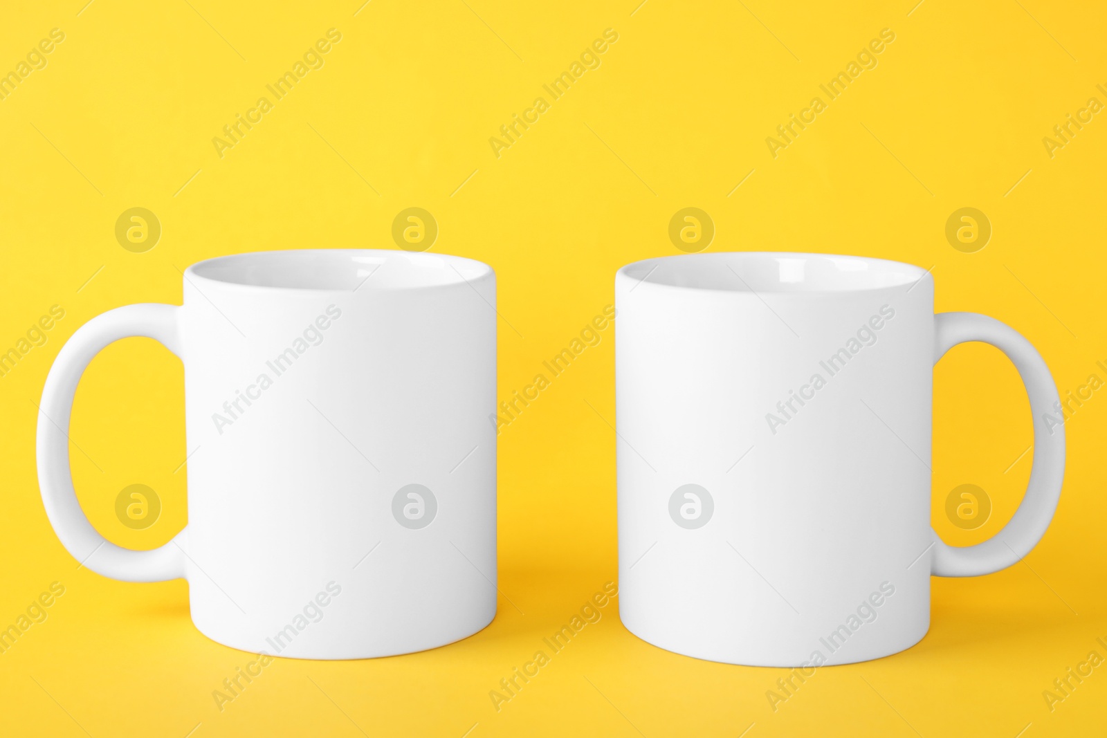 Photo of Two blank white mugs on yellow background. Mockup for design