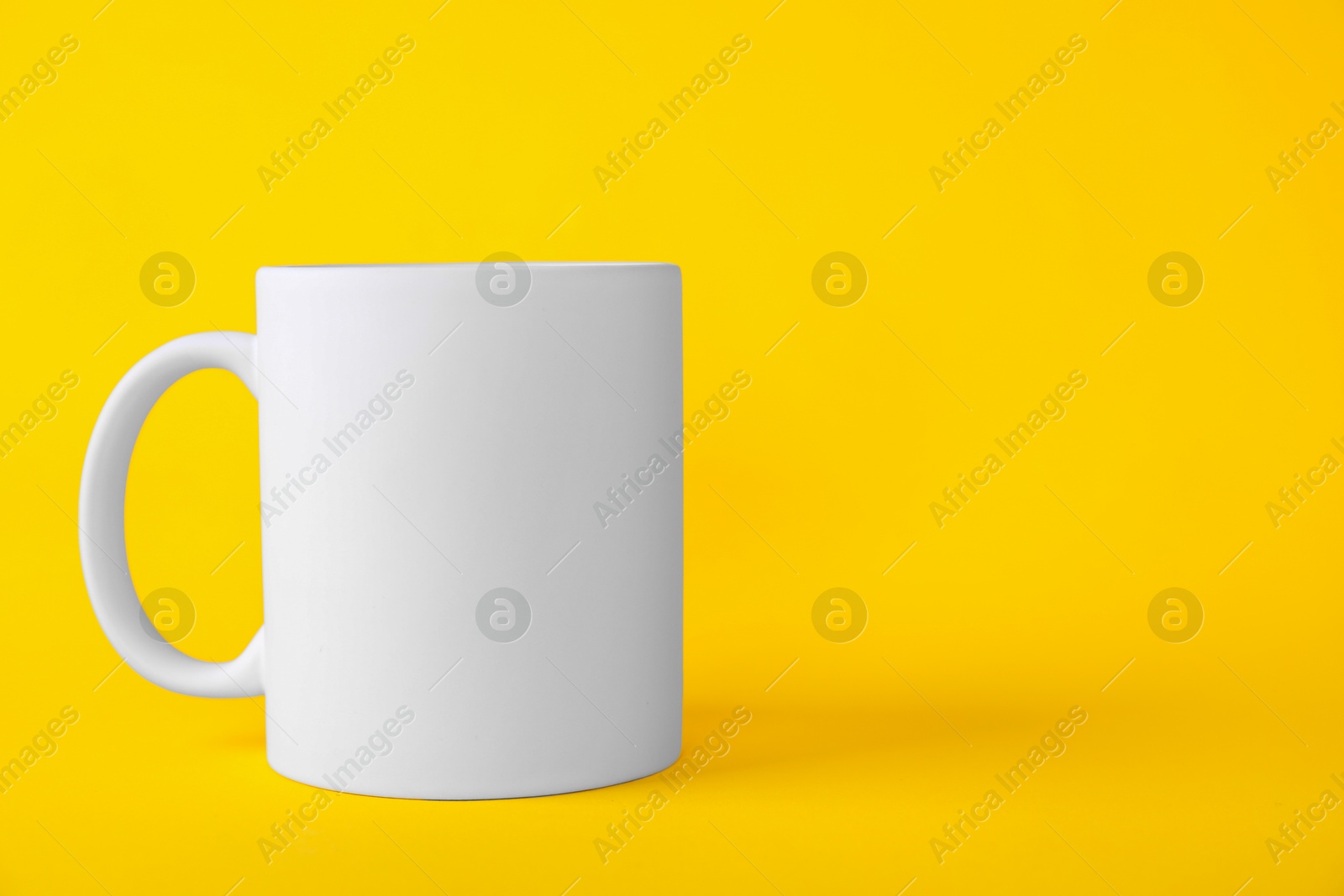 Photo of One blank white mug on yellow background. Mockup for design