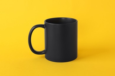 Photo of One blank black mug on yellow background. Mockup for design