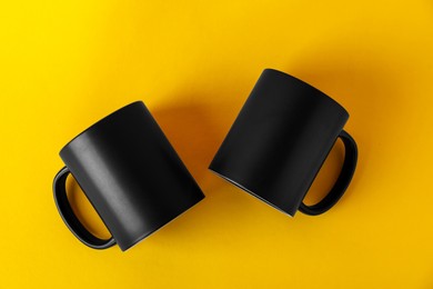 Photo of Two blank black mugs on yellow background, top view. Mockup for design