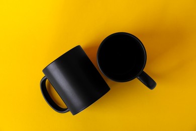 Photo of Two blank black mugs on yellow background, top view. Mockup for design