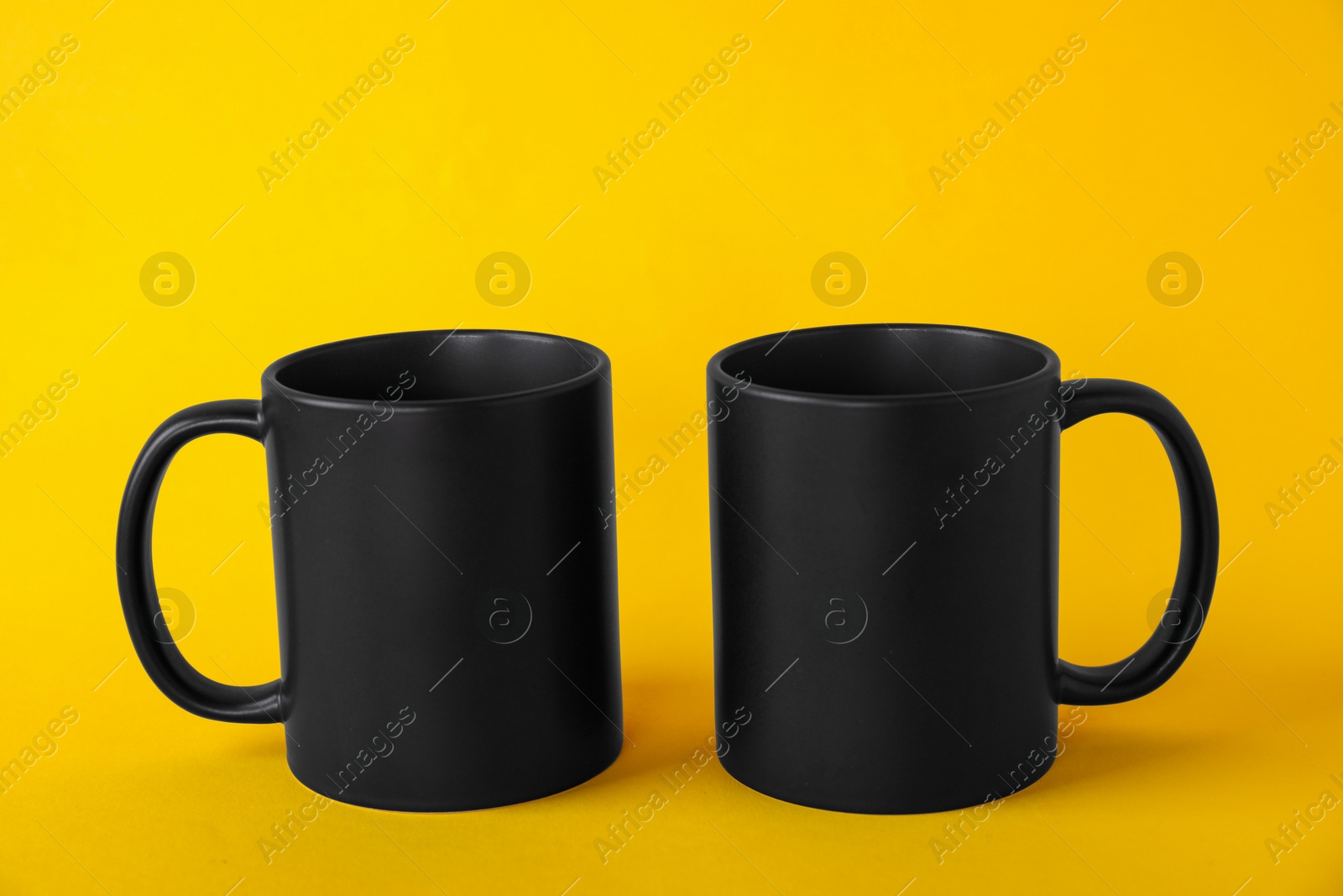 Photo of Two blank black mugs on yellow background. Mockup for design