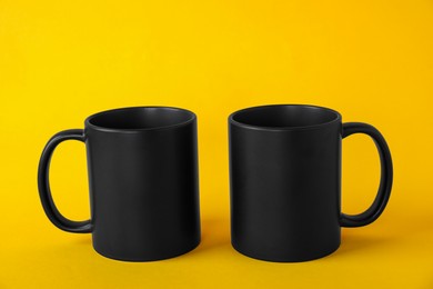 Photo of Two blank black mugs on yellow background. Mockup for design