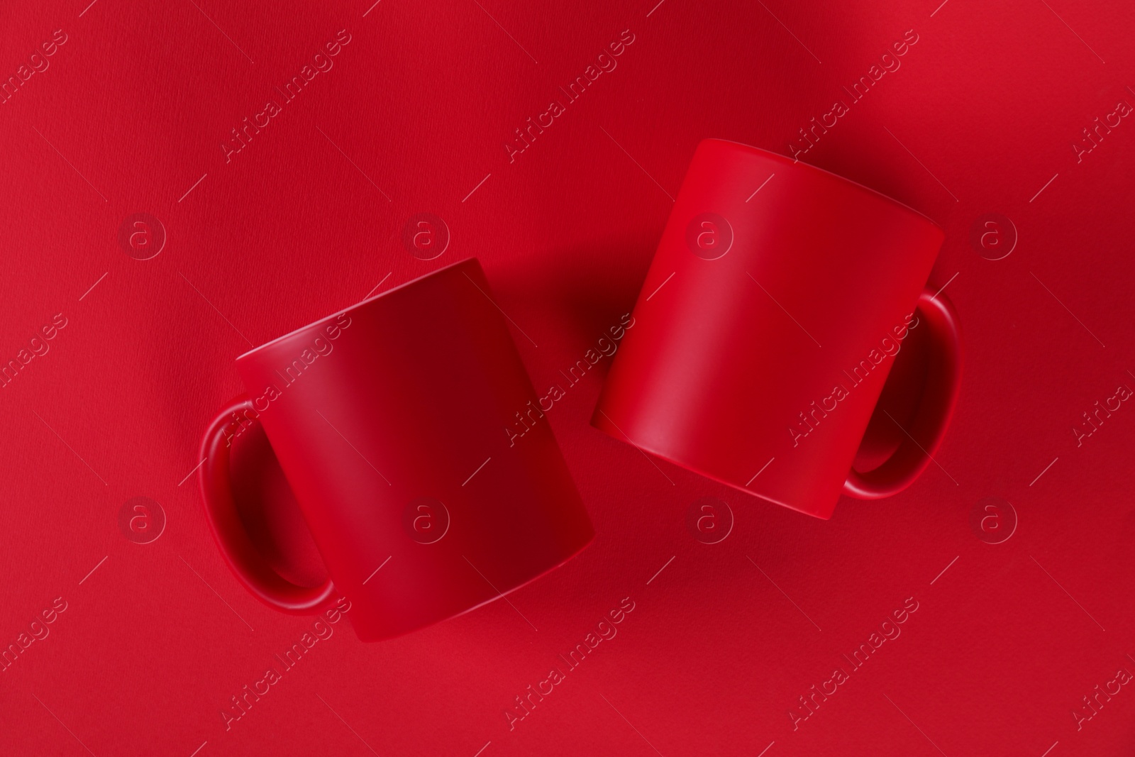 Photo of Two blank mugs on red background, top view. Mockup for design