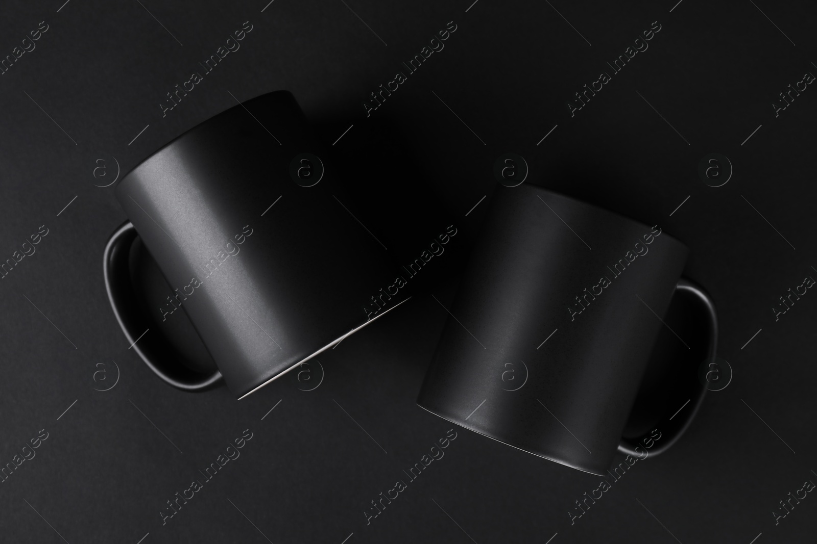 Photo of Two blank mugs on black background, top view. Mockup for design