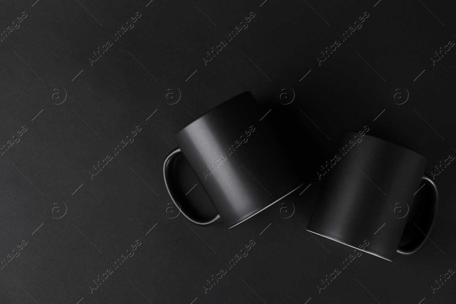 Photo of Two blank mugs on black background, top view. Mockup for design