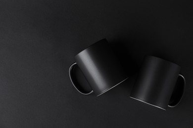 Photo of Two blank mugs on black background, top view. Mockup for design