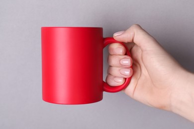 Photo of Woman holding blank red mug on grey background, closeup. Mockup for design