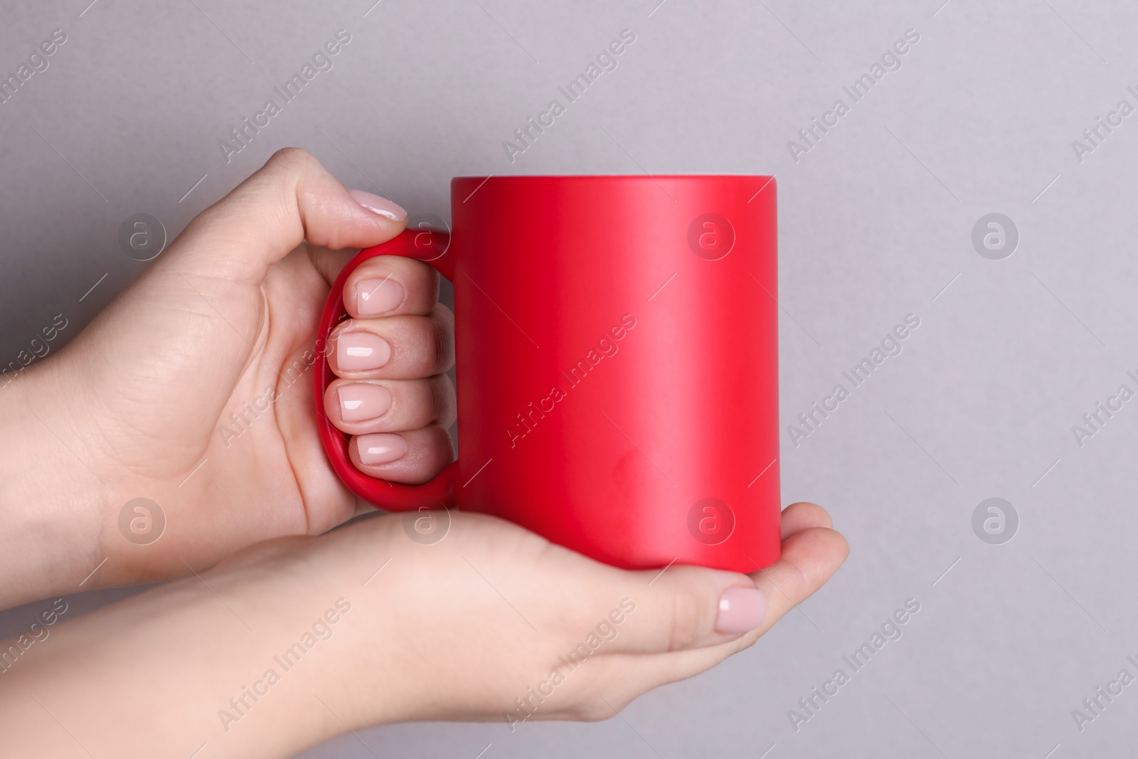 Photo of Woman holding blank red mug on grey background, closeup. Mockup for design