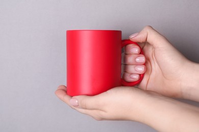 Photo of Woman holding blank red mug on grey background, closeup. Mockup for design