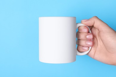 Photo of Woman holding blank white mug on light blue background, closeup. Mockup for design