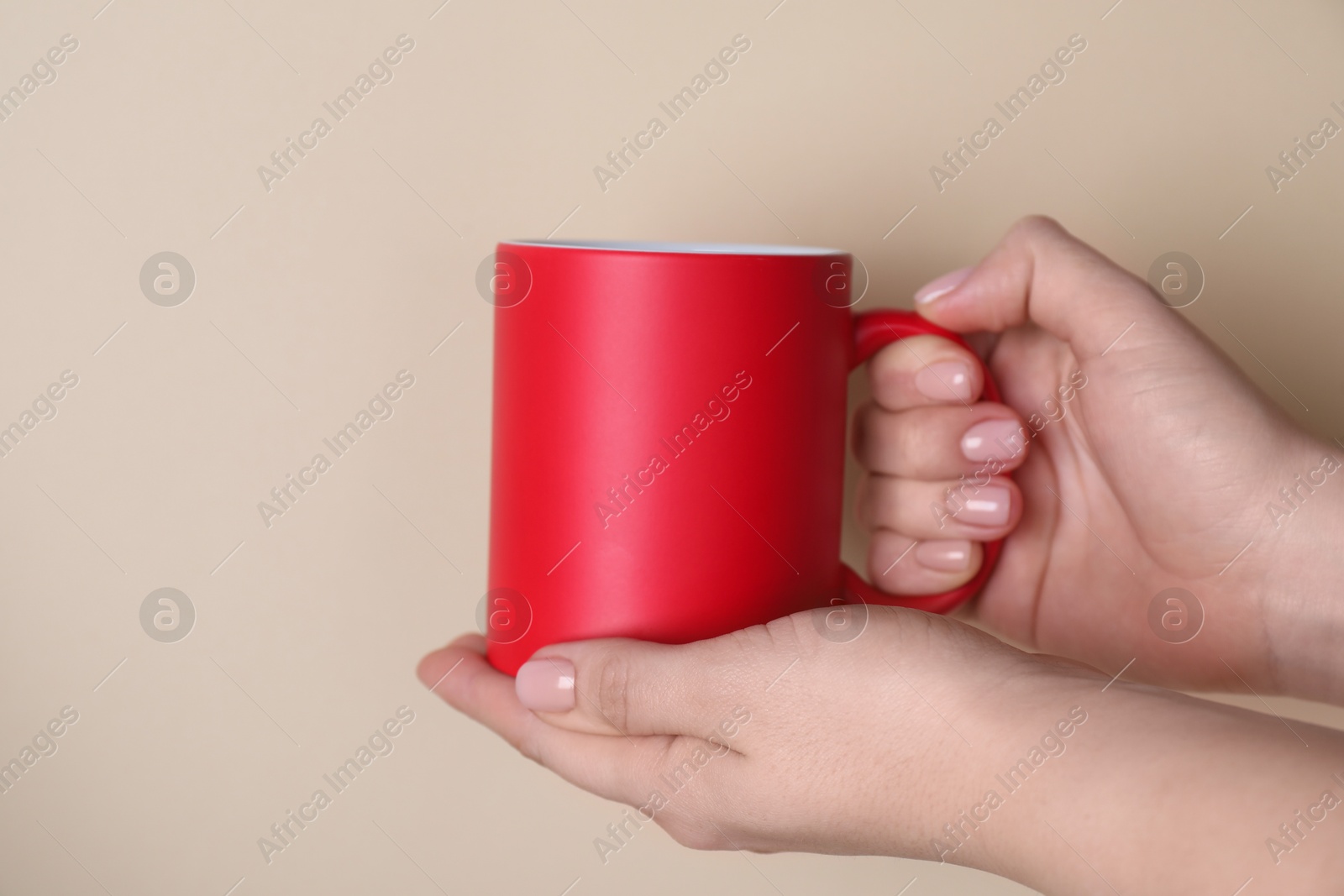 Photo of Woman holding blank red mug on beige background, closeup. Mockup for design