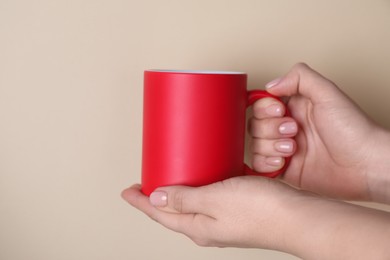 Photo of Woman holding blank red mug on beige background, closeup. Mockup for design