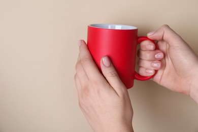 Photo of Woman holding blank red mug on beige background, closeup. Mockup for design