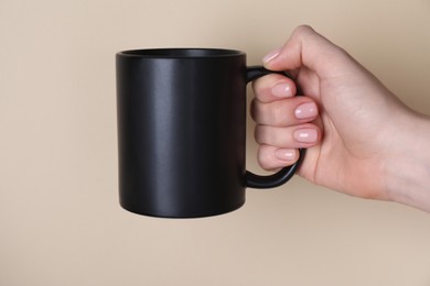 Photo of Woman holding blank black mug on beige background, closeup. Mockup for design