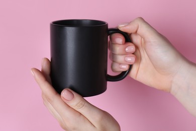 Photo of Woman holding blank black mug on pink background, closeup. Mockup for design