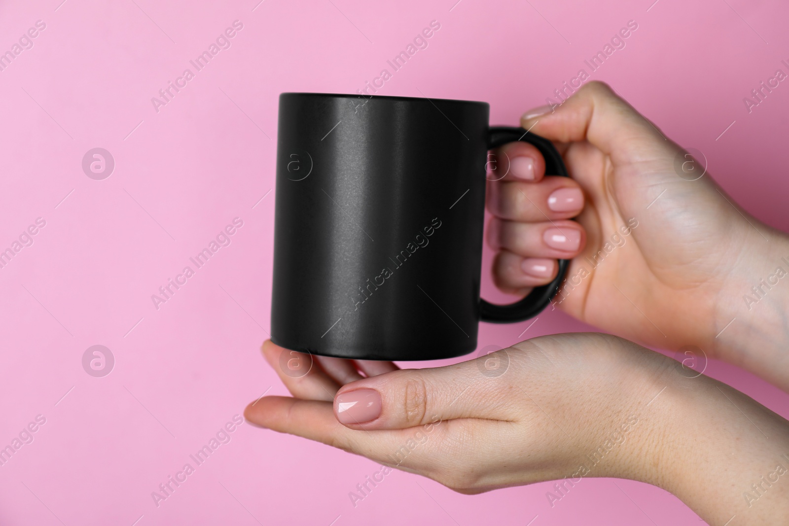 Photo of Woman holding blank black mug on pink background, closeup. Mockup for design