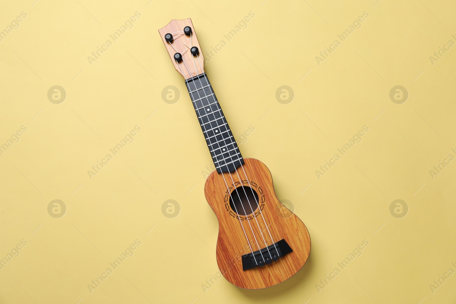 Photo of One ukulele on pale yellow background, top view