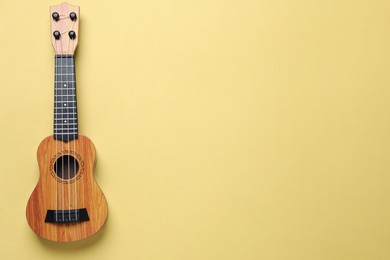 Photo of One ukulele on pale yellow background, top view. Space for text