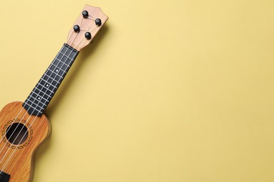 Photo of One ukulele on pale yellow background, top view. Space for text