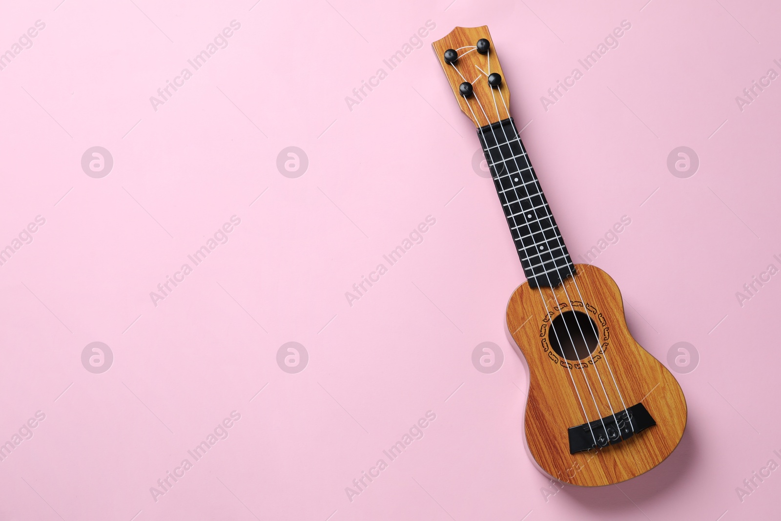 Photo of One ukulele on pink background, top view. Space for text