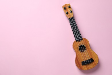 Photo of One ukulele on pink background, top view. Space for text