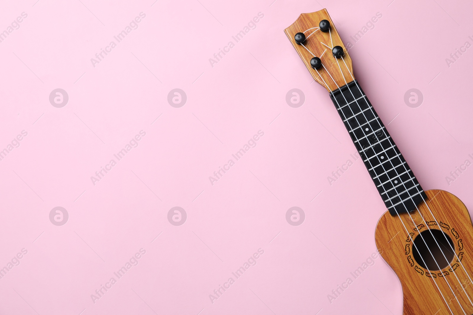 Photo of One ukulele on pink background, top view. Space for text