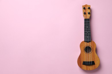 Photo of One ukulele on pink background, top view. Space for text