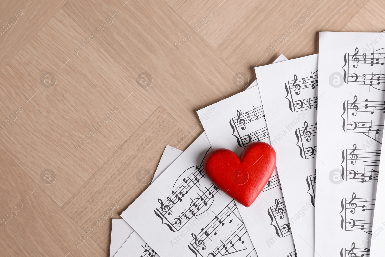 Photo of Heart figure and musical note sheets on wooden table, top view. Space for text