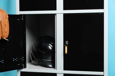 Photo of Open locker with baseball helmet and glove on light blue background, closeup