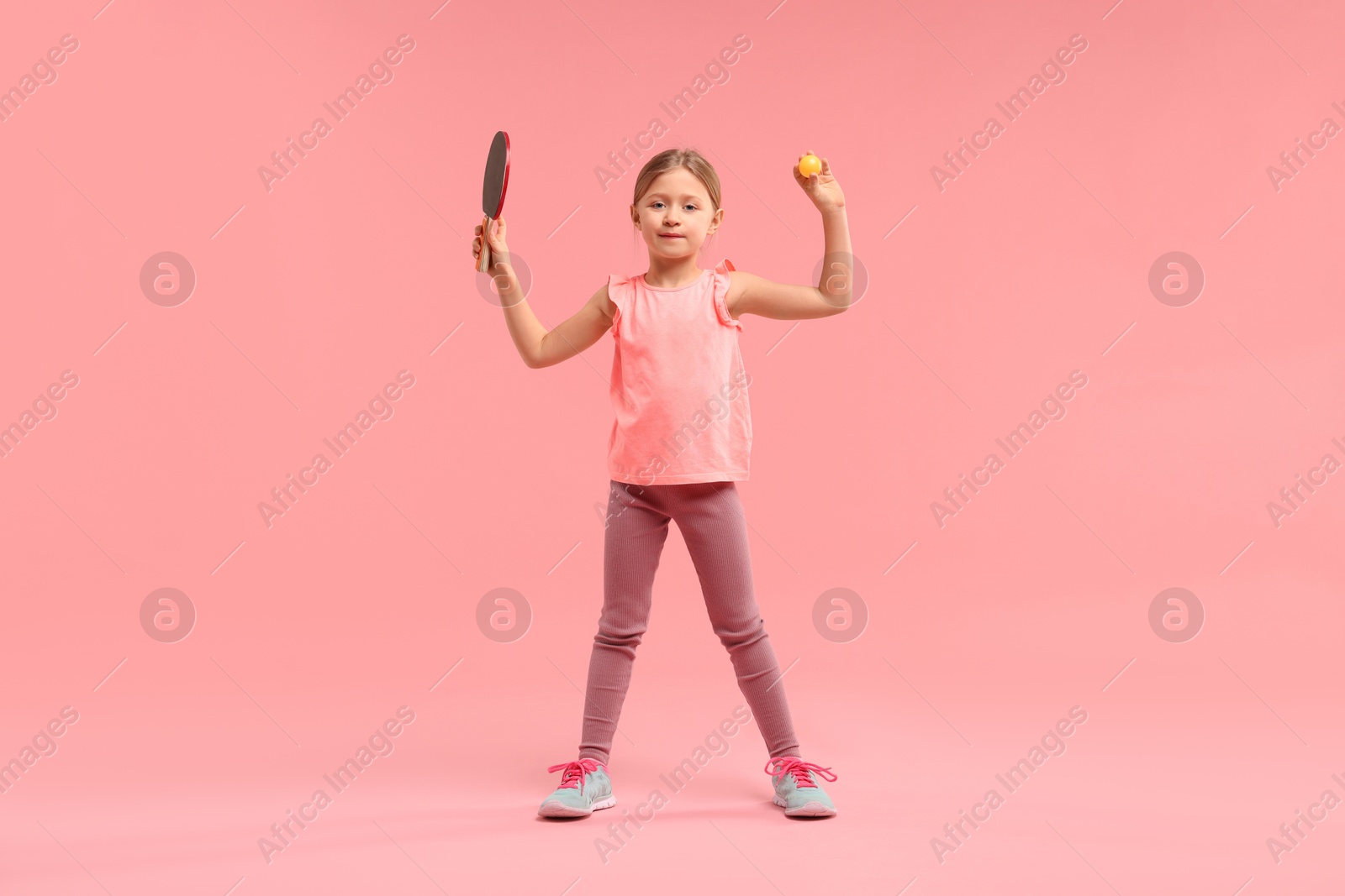 Photo of Cute little girl with ping pong racket and ball on pink background