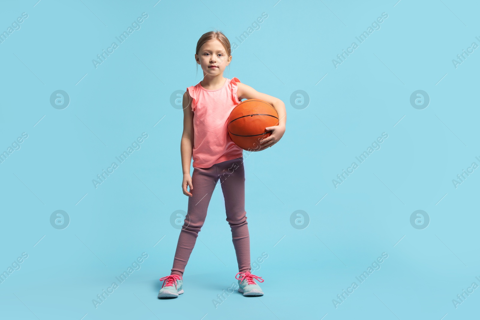 Photo of Cute little girl with basketball ball on light blue background