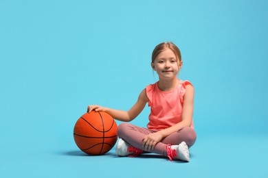 Photo of Cute little girl with basketball ball on light blue background