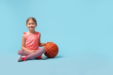 Photo of Cute little girl with basketball ball on light blue background, space for text