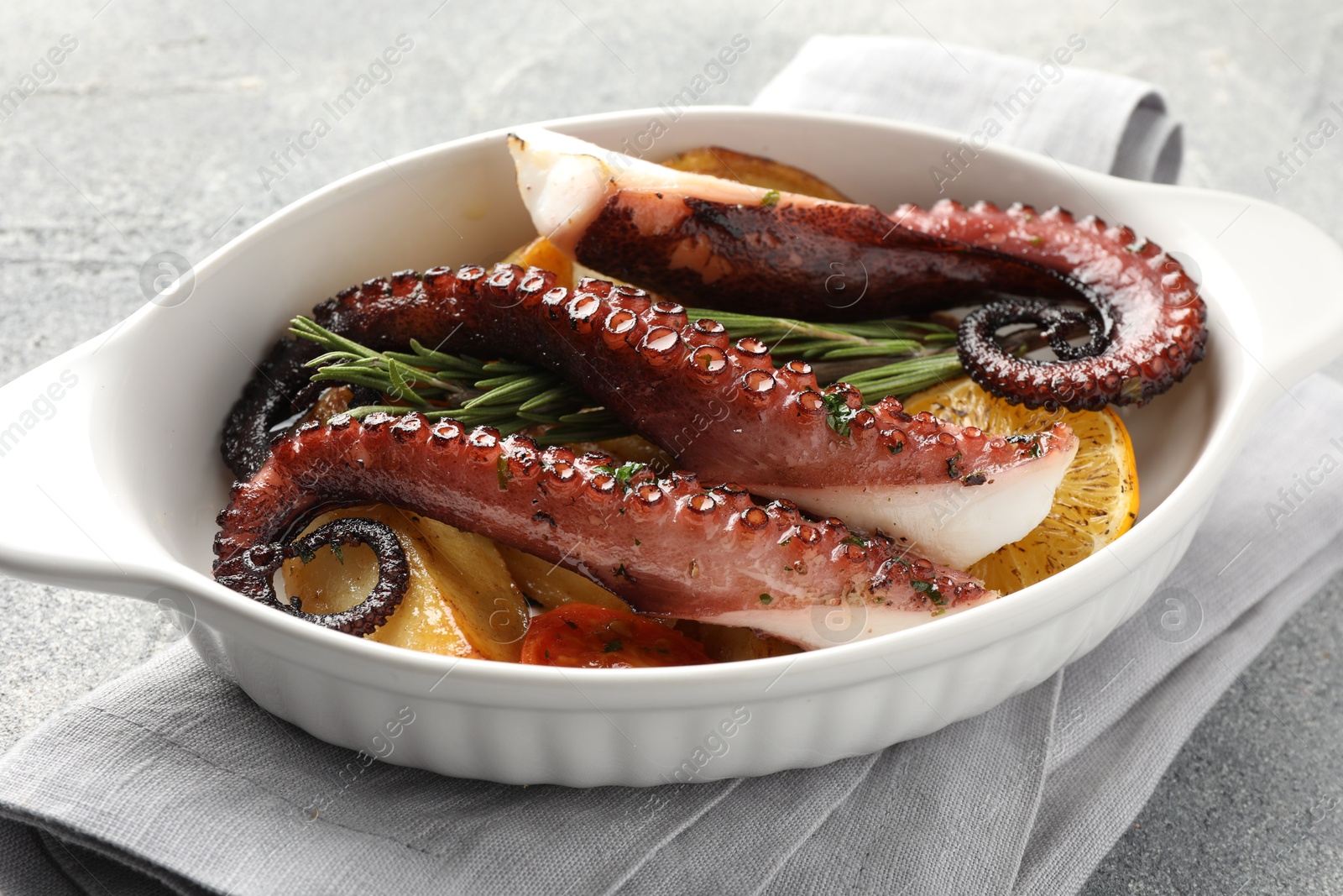 Photo of Fried octopus with vegetables, lemon and rosemary in baking dish on grey textured table, closeup