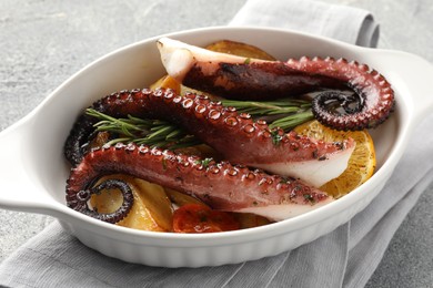 Photo of Fried octopus with vegetables, lemon and rosemary in baking dish on grey textured table, closeup