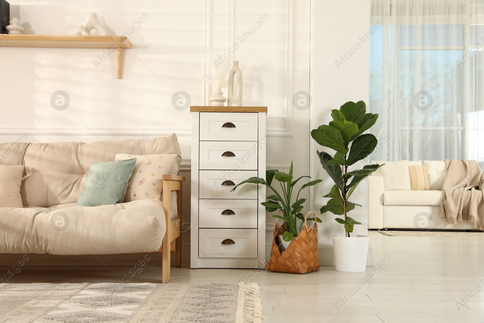 Photo of Beautiful sofa with cushions, commode and houseplants in living room. Interior design