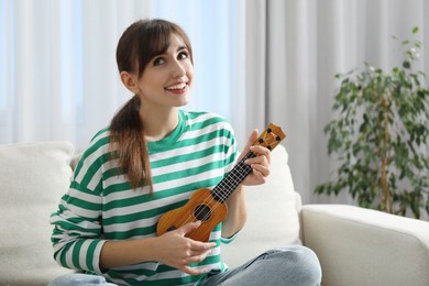 Photo of Happy woman playing ukulele on sofa at home