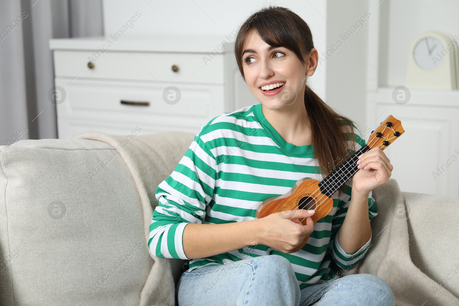 Photo of Happy woman playing ukulele on sofa at home