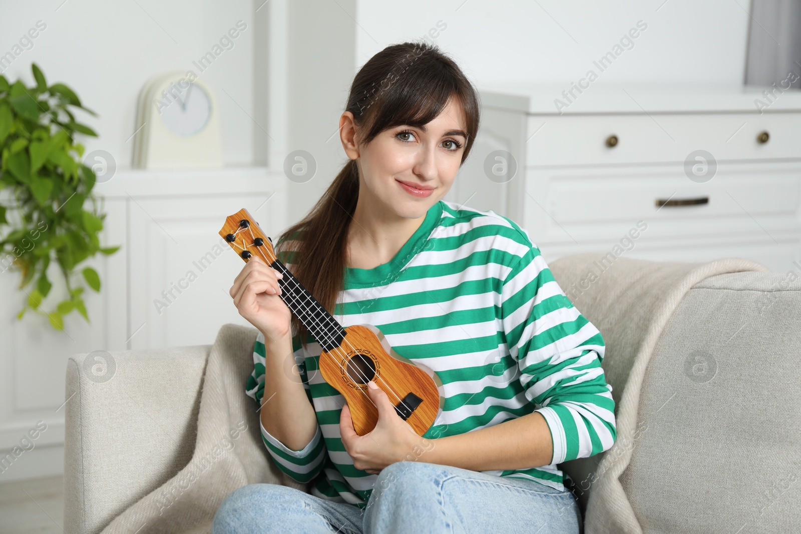 Photo of Happy woman playing ukulele on sofa at home