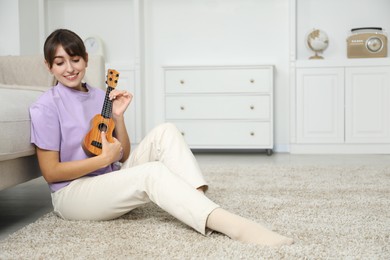 Photo of Happy woman playing ukulele on floor at home, space for text