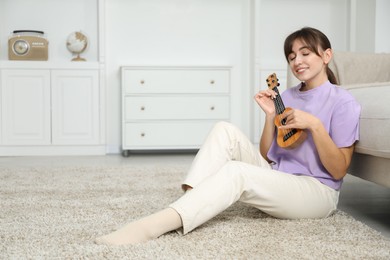 Photo of Happy woman playing ukulele on floor at home, space for text