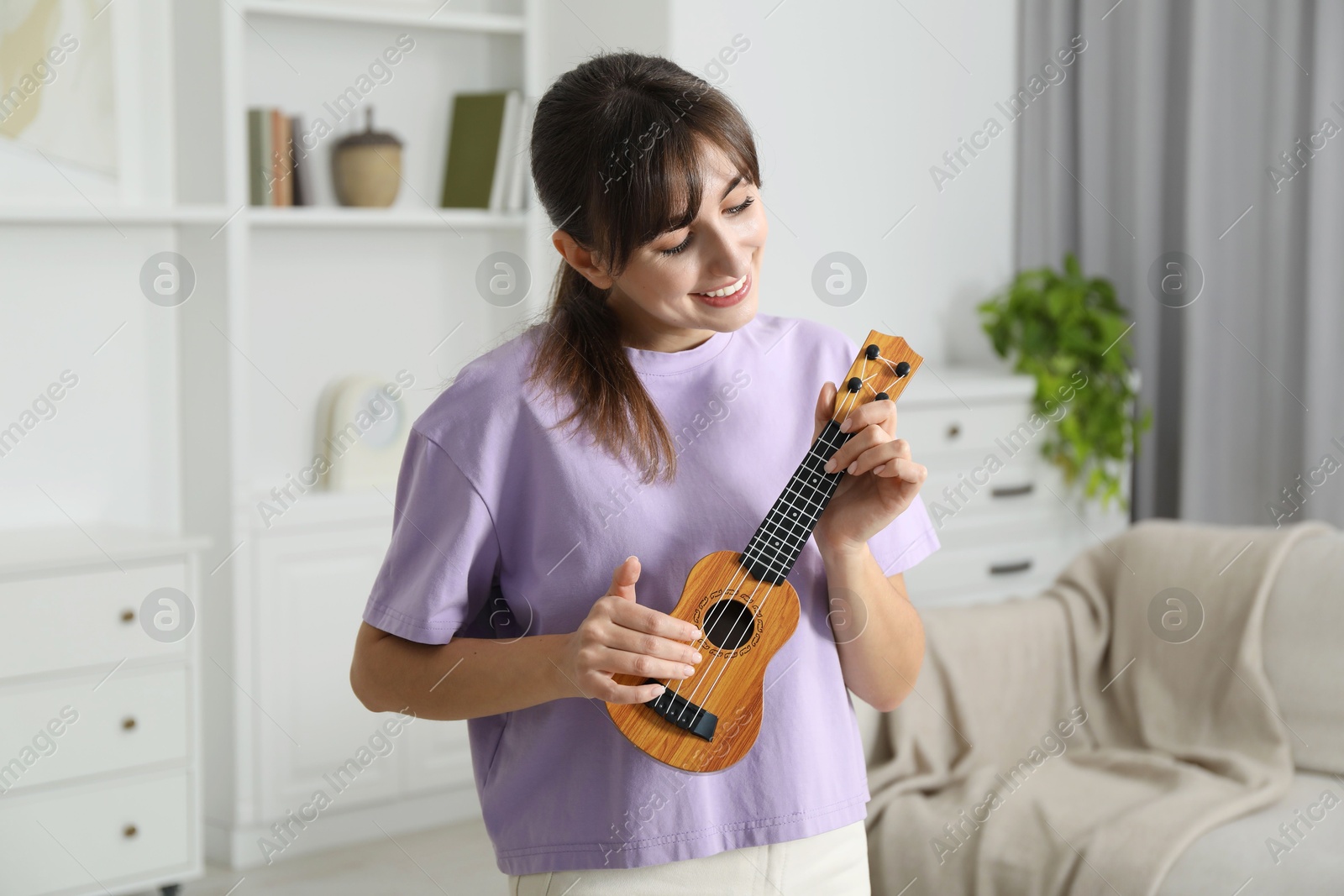 Photo of Happy young woman playing ukulele at home